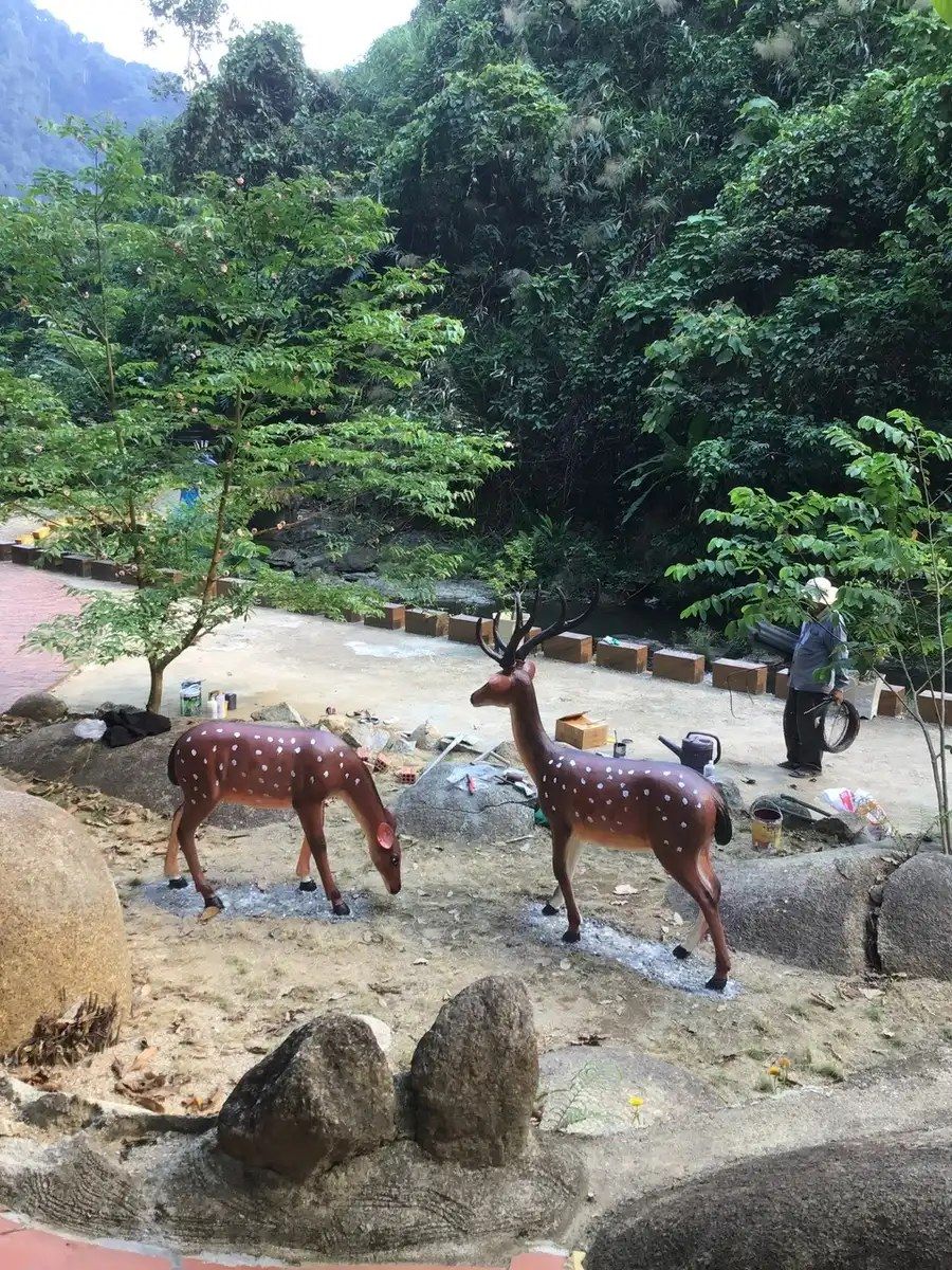 Tượng hươu nai xi măng đặt trong tiểu cảnh suối đá tự nhiên, cây xanh bao quanh